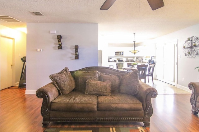 living room featuring hardwood / wood-style flooring, a textured ceiling, and ceiling fan