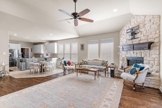 living room with a stone fireplace, ceiling fan, light hardwood / wood-style floors, and vaulted ceiling