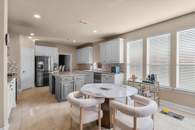 kitchen featuring light stone countertops, tasteful backsplash, stainless steel appliances, white cabinets, and a kitchen island