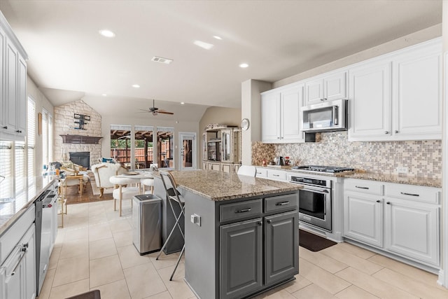 kitchen with white cabinetry, stainless steel appliances, vaulted ceiling, a fireplace, and a kitchen island