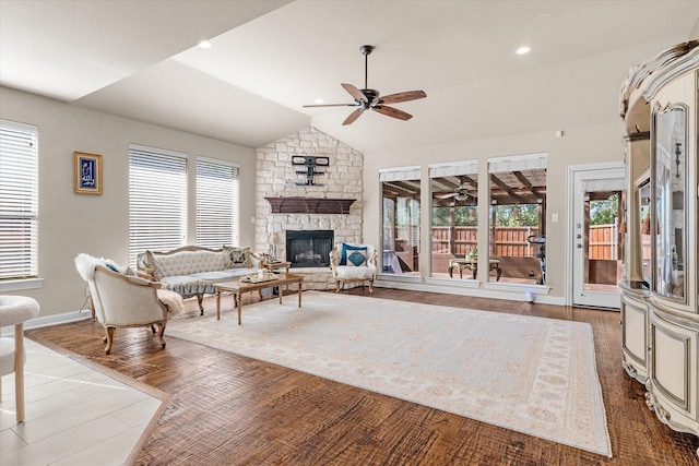 living room with wood-type flooring, vaulted ceiling, a healthy amount of sunlight, and a stone fireplace