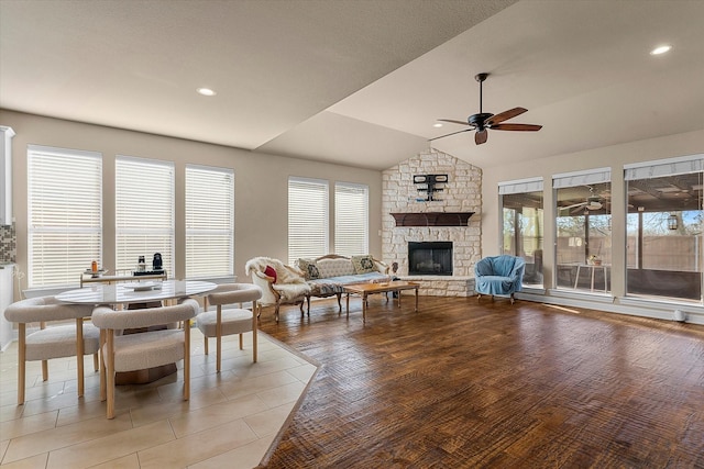 dining room with ceiling fan, light wood-type flooring, a fireplace, and vaulted ceiling