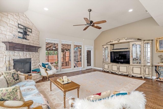 living room with hardwood / wood-style floors, vaulted ceiling, a stone fireplace, and ceiling fan