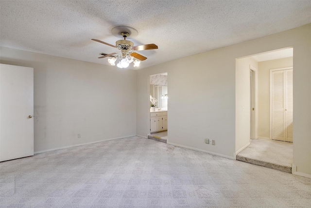 unfurnished room featuring ceiling fan, light colored carpet, and a textured ceiling