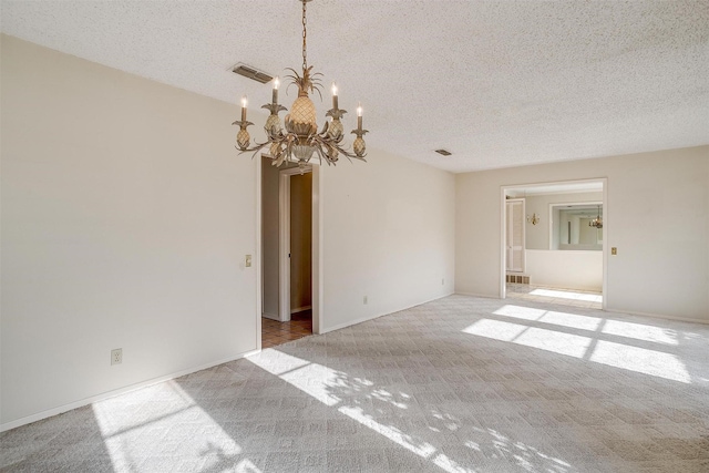 empty room with light colored carpet, a textured ceiling, and a chandelier