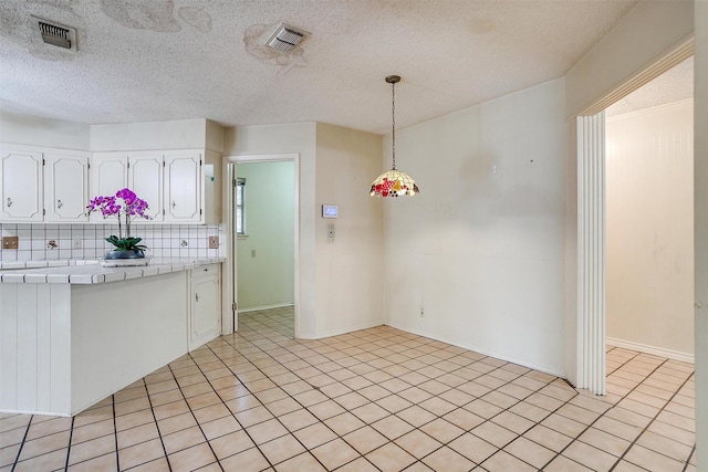 kitchen featuring decorative backsplash, a textured ceiling, pendant lighting, tile countertops, and white cabinetry