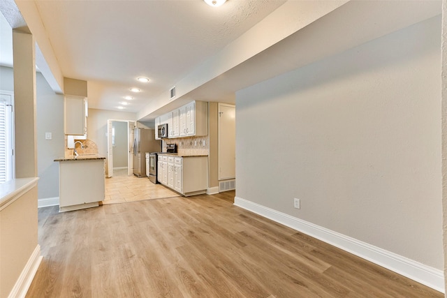 kitchen with decorative backsplash, stainless steel appliances, white cabinetry, and light hardwood / wood-style flooring