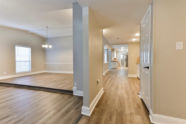 hallway featuring light hardwood / wood-style flooring, a chandelier, and lofted ceiling