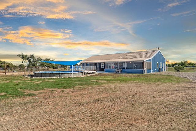 back house at dusk with a lawn and a sunroom