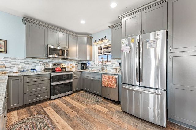 kitchen featuring gray cabinetry, dark hardwood / wood-style floors, light stone countertops, appliances with stainless steel finishes, and tasteful backsplash