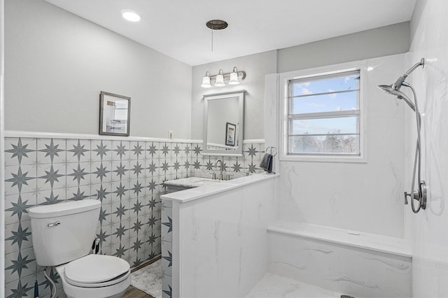 bathroom featuring a shower, vanity, toilet, and tile walls