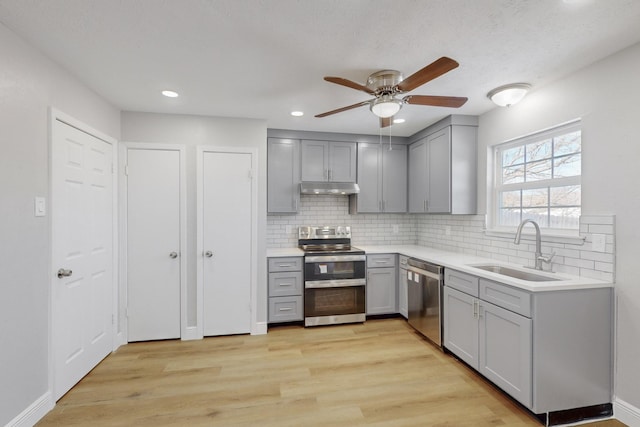 kitchen with gray cabinetry, backsplash, sink, light wood-type flooring, and appliances with stainless steel finishes