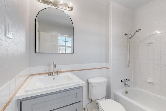 full bathroom featuring tiled shower / bath, vanity, tile walls, and toilet