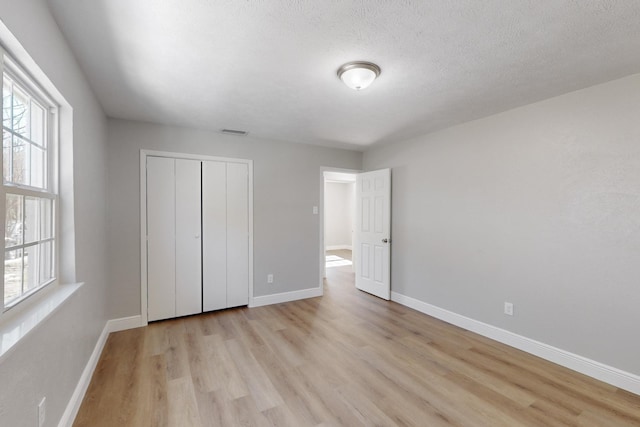 unfurnished bedroom with light wood-type flooring, a textured ceiling, and a closet