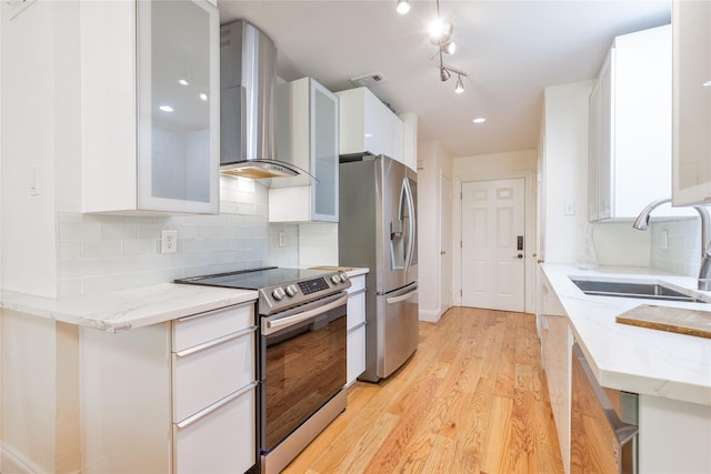 kitchen featuring wall chimney exhaust hood, white cabinets, light stone counters, and appliances with stainless steel finishes