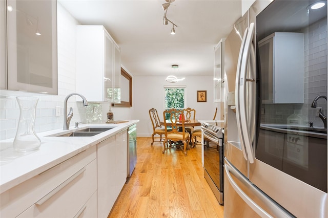 kitchen with appliances with stainless steel finishes, white cabinets, light hardwood / wood-style flooring, backsplash, and sink