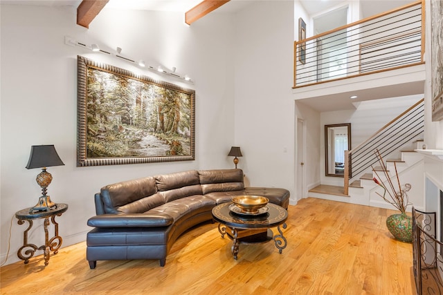 living room with light wood-type flooring, a towering ceiling, and beamed ceiling