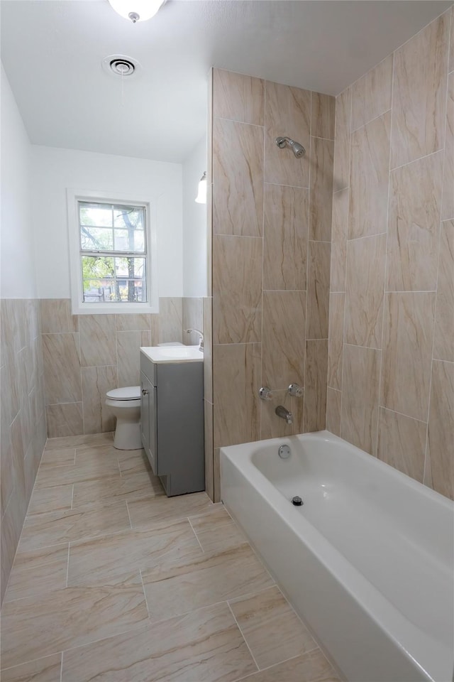 full bathroom featuring vanity, tiled shower / bath combo, tile walls, tile patterned flooring, and toilet