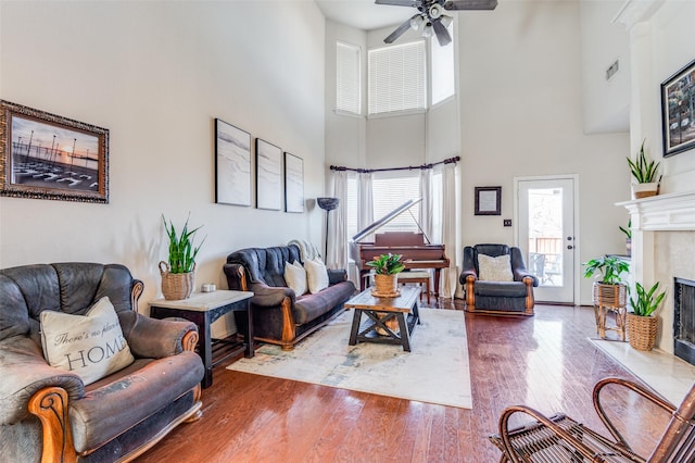 living room with ceiling fan, wood-type flooring, a towering ceiling, and a fireplace