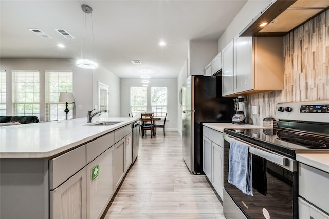 kitchen with appliances with stainless steel finishes, a kitchen island with sink, sink, white cabinetry, and hanging light fixtures