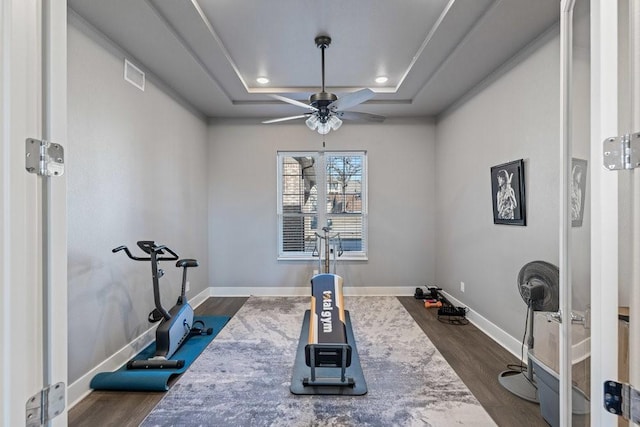 exercise area with a tray ceiling, dark hardwood / wood-style floors, and ceiling fan