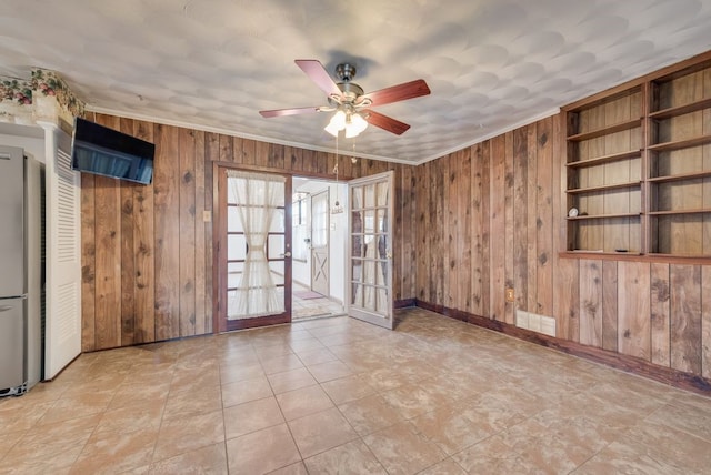 unfurnished room featuring ceiling fan, wood walls, crown molding, and french doors