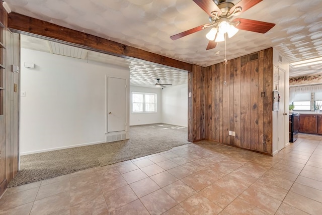 unfurnished room with beamed ceiling, ceiling fan, light colored carpet, and wooden walls