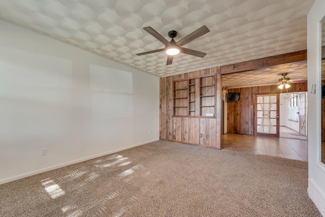 empty room featuring carpet flooring, ceiling fan, wood walls, and french doors