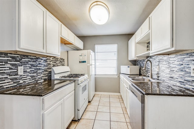 kitchen with dark stone counters, white appliances, sink, light tile patterned floors, and white cabinetry