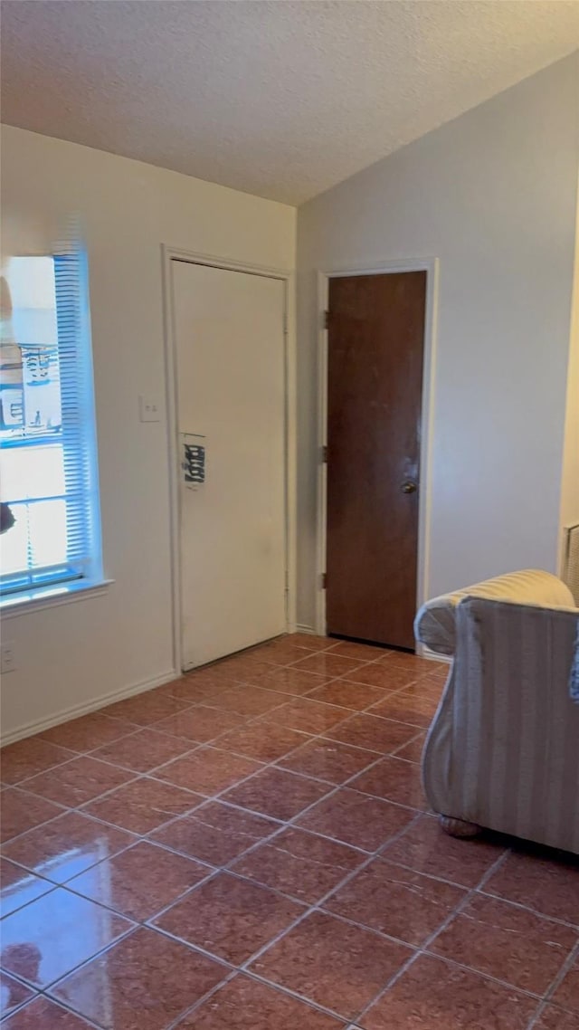 entrance foyer with a textured ceiling, lofted ceiling, and dark tile patterned flooring