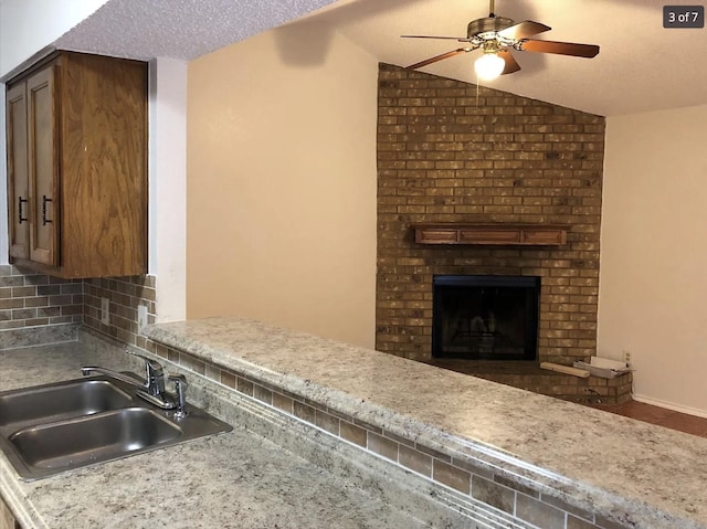 kitchen with lofted ceiling, backsplash, sink, a brick fireplace, and a textured ceiling