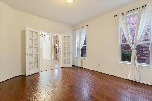 unfurnished room featuring a wealth of natural light, french doors, wood-type flooring, and a notable chandelier