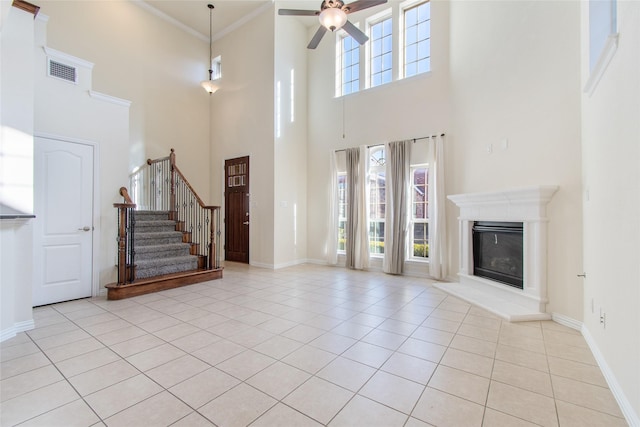 unfurnished living room with light tile patterned floors, ceiling fan, ornamental molding, and a high ceiling