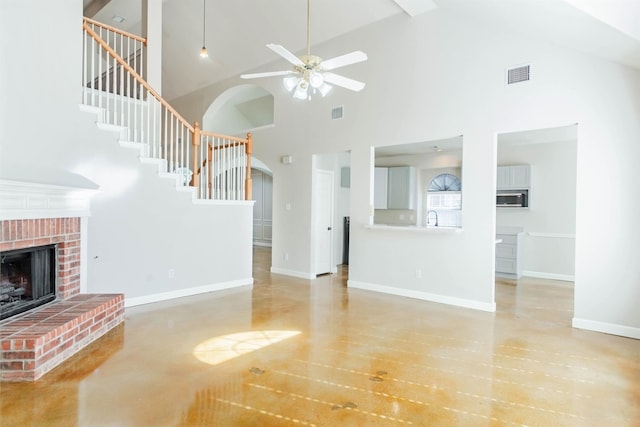 unfurnished living room featuring ceiling fan, a fireplace, a high ceiling, and sink