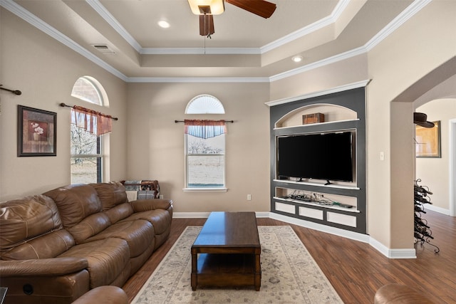 living room with a raised ceiling, ceiling fan, dark wood-type flooring, and ornamental molding