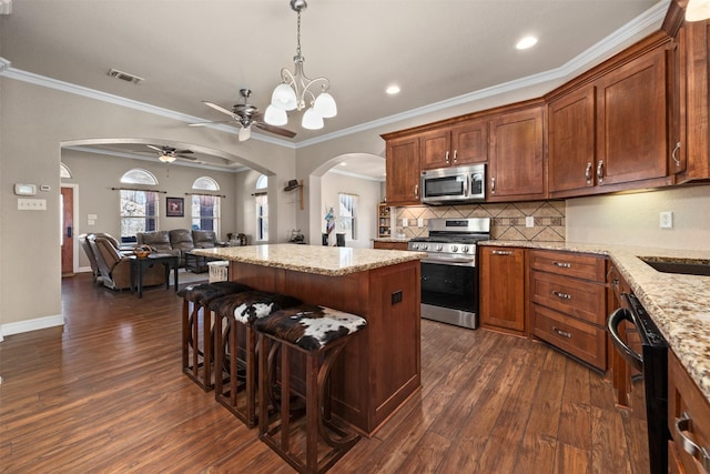 kitchen featuring light stone countertops, appliances with stainless steel finishes, backsplash, ornamental molding, and a kitchen island