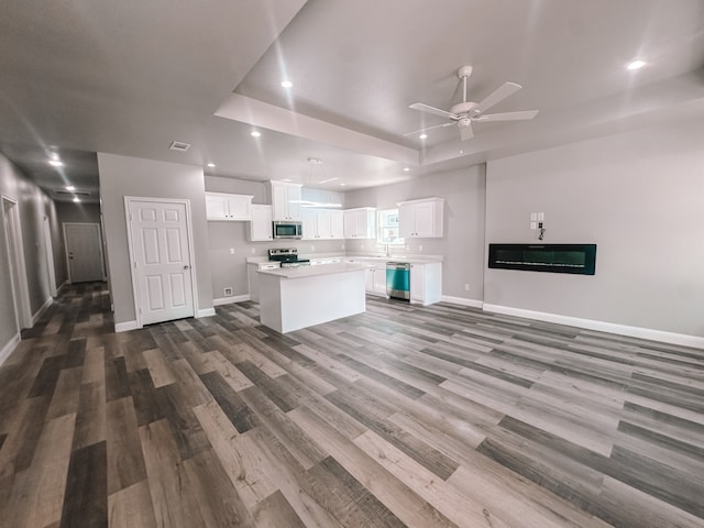 unfurnished living room with ceiling fan, a raised ceiling, and dark wood-type flooring