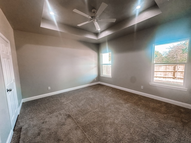 unfurnished room featuring ceiling fan, a raised ceiling, carpet floors, and a wealth of natural light