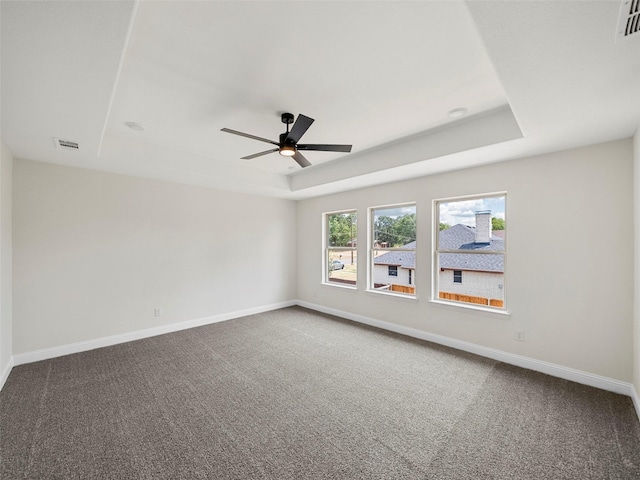 carpeted spare room featuring visible vents, a tray ceiling, a ceiling fan, and baseboards