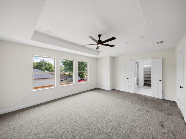 carpeted spare room featuring a ceiling fan, a raised ceiling, visible vents, and baseboards