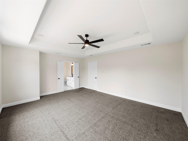 carpeted empty room featuring a ceiling fan, a raised ceiling, visible vents, and baseboards