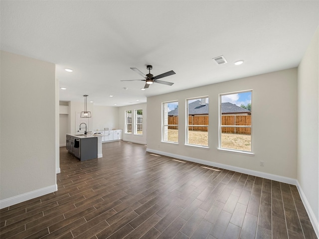 unfurnished living room featuring a sink, baseboards, visible vents, and dark wood-type flooring