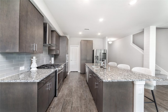 kitchen with wall chimney exhaust hood, a kitchen island with sink, a breakfast bar, and appliances with stainless steel finishes