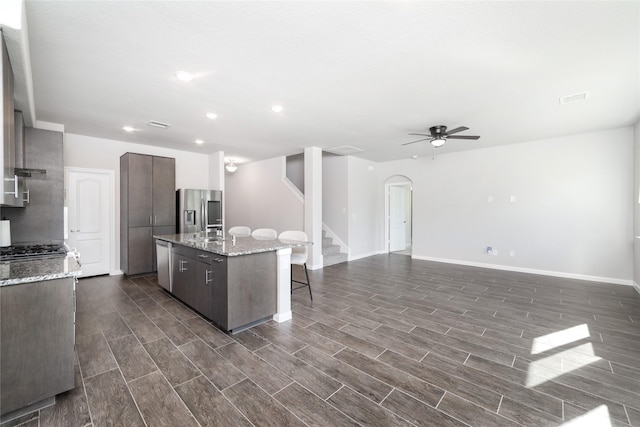 kitchen with a kitchen island with sink, ceiling fan, a kitchen bar, dark brown cabinetry, and stainless steel appliances