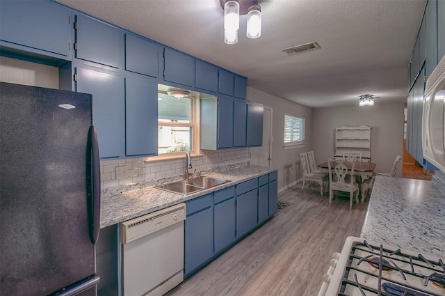 kitchen featuring dishwasher, sink, black fridge, blue cabinets, and decorative backsplash