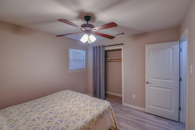 bedroom with ceiling fan, light hardwood / wood-style floors, a textured ceiling, and a closet