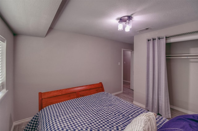 bedroom with a textured ceiling, light wood-type flooring, and a closet