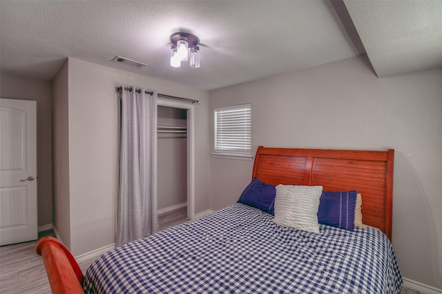 bedroom with light hardwood / wood-style floors, a textured ceiling, and a closet