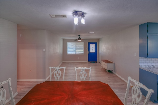 unfurnished dining area with ceiling fan, light wood-type flooring, and a textured ceiling