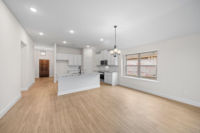 kitchen featuring tasteful backsplash, decorative light fixtures, a kitchen island with sink, white cabinets, and appliances with stainless steel finishes